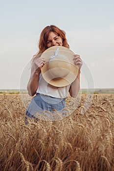 Woman with hat in her hands in summer field golden wheat, beautiful happy girl with golden brown hair, enjoying life.