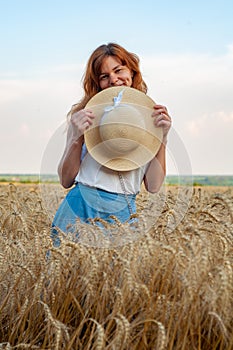 Woman with hat in her hands in summer field golden wheat, beautiful happy girl with golden brown hair, enjoying life.