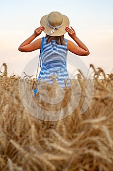 Woman with hat in her hands in summer field golden wheat, beautiful happy girl with golden brown hair, enjoying life.