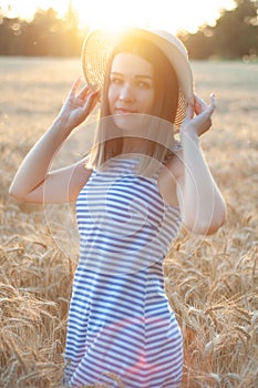 Woman with hat in her hands in summer field golden wheat, beautiful happy girl with golden brown hair, enjoying life.