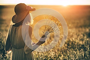 Woman with hat holding grass herb bouquet in summer field