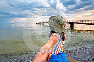 Woman in hat holding man hand on sea beach on relax holiday vacation. Follow me