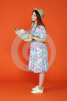 Woman in hat holding paper map, confused face expression, looking searching right direction, isolated on orange