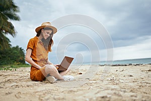 woman in hat with laptop sitting on the beach vacation island