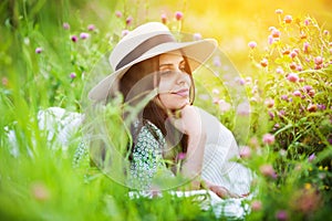 Woman in a hat lies on the grass among a field clover