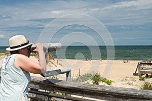 Woman in  hat looks through Coin binoculars at ocean