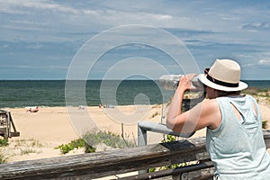 Woman in  hat looks through Coin binoculars at ocean