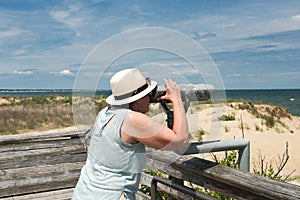 Woman in a hat looks through Coin binoculars at ocean