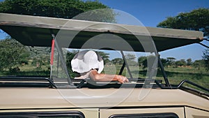 Woman In Hat Looks At Wild Animals In Reserve From Roof Hatch Of A Safari Jeep