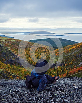 A woman in a hat on a mountain slope looks through binoculars in autumn against the backdrop of a lake and mountains