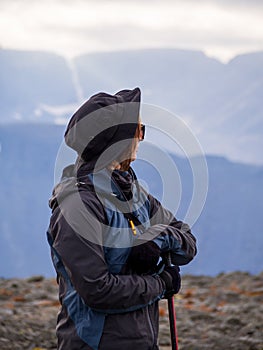 A woman in a hat on a mountain slope looks through binoculars in autumn against the backdrop of a lake and mountains