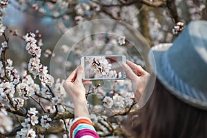 Woman in hat photographed on a smartphone flowering spring tree