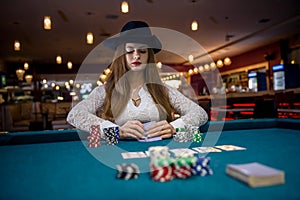 Woman in hat with playing cards and poker chips in casino