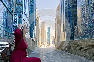 Woman with hat and red dress relaxing on the bench and enjoying the beauty of the ancient Shah-i-Zinda complex, Samarkand,