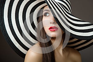 Woman in a hat and with red lips. Portrait of a young beautiful brunette. Dark background