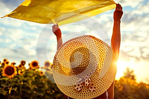 Woman in hat relaxing in blooming sunflower field raised arms with scarf and having fun. Free and happy. Summer vacation