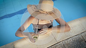 Woman in hat relaxing at pool with cosmopolitan cocktail