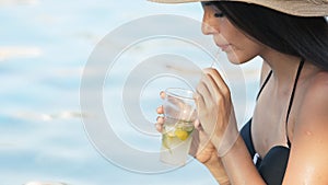 Woman in hat relaxing at pool with cosmopolitan cocktail