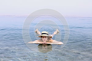 Woman with hat relaxing in salty water of a Dead Sea