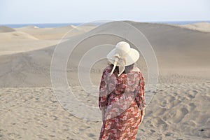 Woman with a hat on the sand dunes watching the horizon