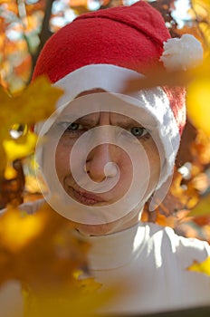 A woman in a hat of Santaclaus with a sly evil face among the autumn foliage as a harbinger of the coming winter.