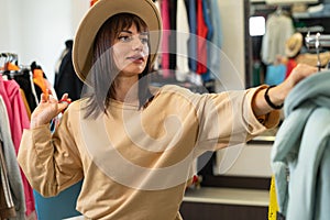 woman in a hat shopping in the clothing department of a mall, a girl choosing clothes on the hangers of a store, buying