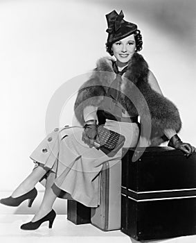 Woman with a hat sitting on suitcases and smiling