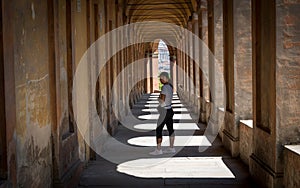 Woman in hat standing in portico with shadows and looking back