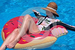 Woman in hat and surfer swimsuit floating with in swimming pool sunny summer day