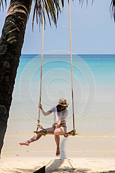 A woman in a hat on a swing on the shore of the turquoise sea