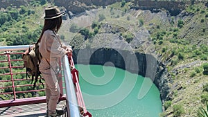 a woman in a hat and travel clothes stands on a precipice of a kimberlite pipe