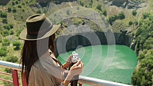 a woman in a hat and travel clothes stands on a precipice of a kimberlite pipe