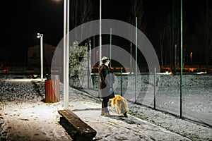 Woman walks at night with the dog on a leash lit by the light of