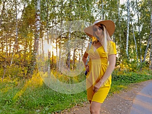 Woman in hat and yellow dress walking at forest