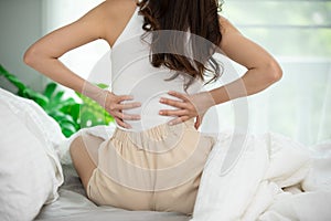 Woman have a back pain sitting on bed in bedroom feeling painful