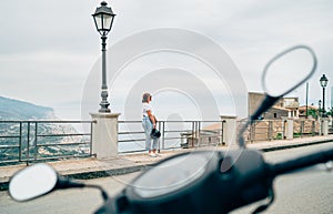 Woman have moto scooter riding break. Female standing on Forza d`Agro Sicilian old town street, enjoying Ionian Seaside coast