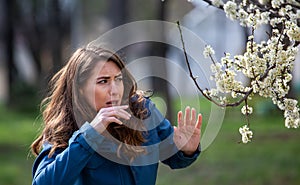 Woman having allergy symptoms in front of blooming tree