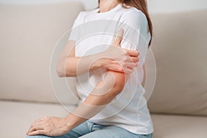 Woman having arm pain during sitting on couch at home, muscle injury and ache. Health and medical concept