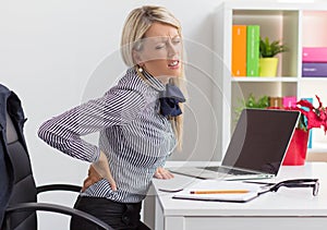 Woman having back pain while sitting at desk in office