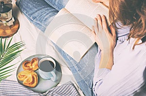 Woman having breakfast in bed and reading a book