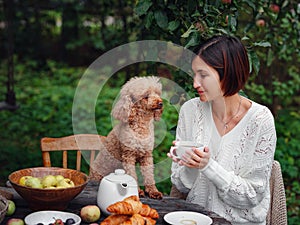 woman having breakfast in garden with her faithful pet poodle.