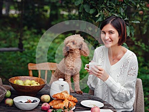 woman having breakfast in garden with her faithful pet poodle.