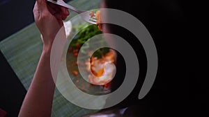 Woman is having breakfast at home, eating scrambled eggs with salad greens, using fork