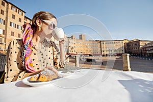 Woman having breakfast at outdoor cafe with beautiful view on main square of Siena city, Italy