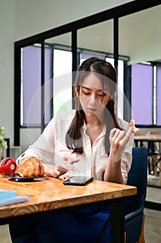 Woman having breakfast and using smart phone at her office room.