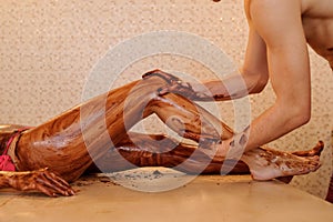 woman having a chocolate massage on her legs done by a man