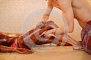 woman having a chocolate massage on her legs done by a man