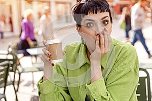 woman having coffee at the street cafe outside, talking with friend aand in shock from information, having fun time.