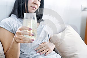 woman having flatulence drinking a glass of fruit salt for relief indigestion, acidity problem hand holding her stomach ache