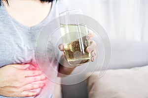 Woman having flatulence drinking a glass of fruit salt for relief indigestion, acidity problem hand holding her stomach ache photo